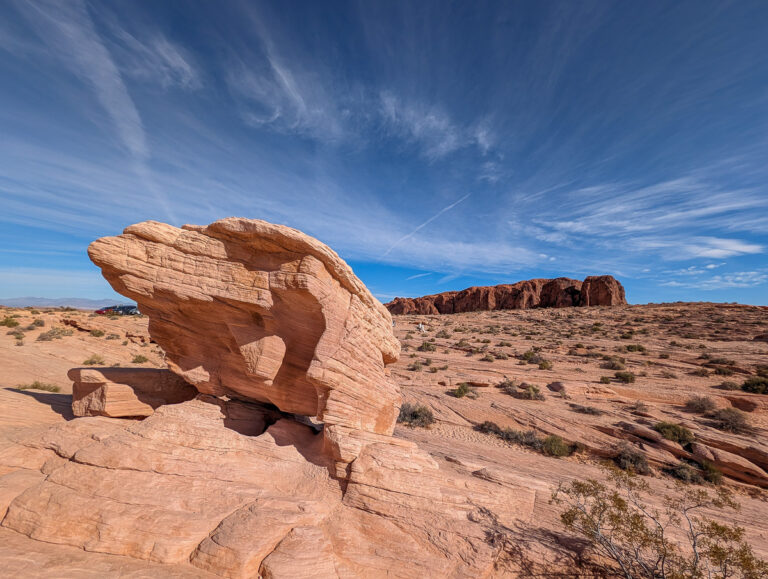A striking desert scene featuring a large sandstone formation, open terrain, and distant rock cliffs under a vibrant sky.