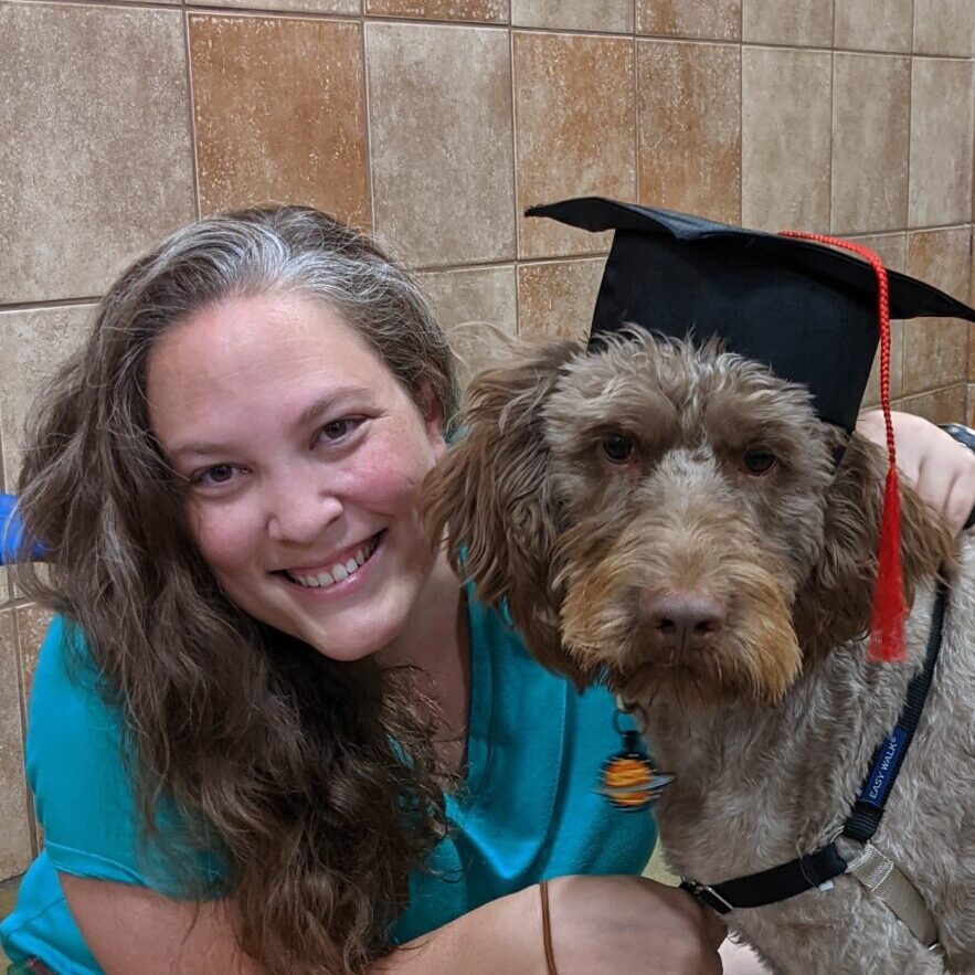 Kristin with her labradoodle, Tycho, in a graduation cap.