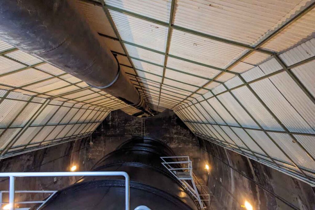 Huge black pipes run through an enclosed industrial passage inside Hoover Dam. Metal railings and ladders reveal part of the infrastructure seen during the dam power plant tour.