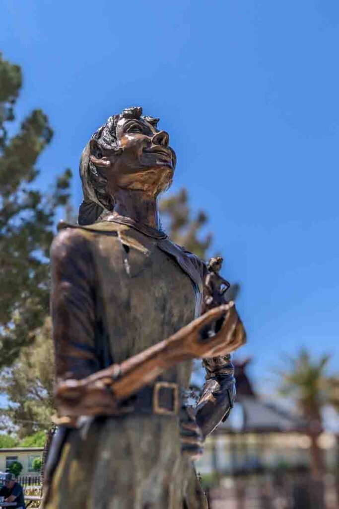 Bronze Peter Pan statue holding Tinkerbell, set against a clear blue sky in downtown Boulder City.